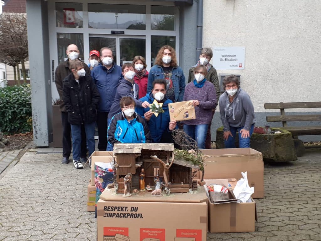 Eine Gruppe von Maskierten posiert draußen mit Kartons und einem Modellhaus.
