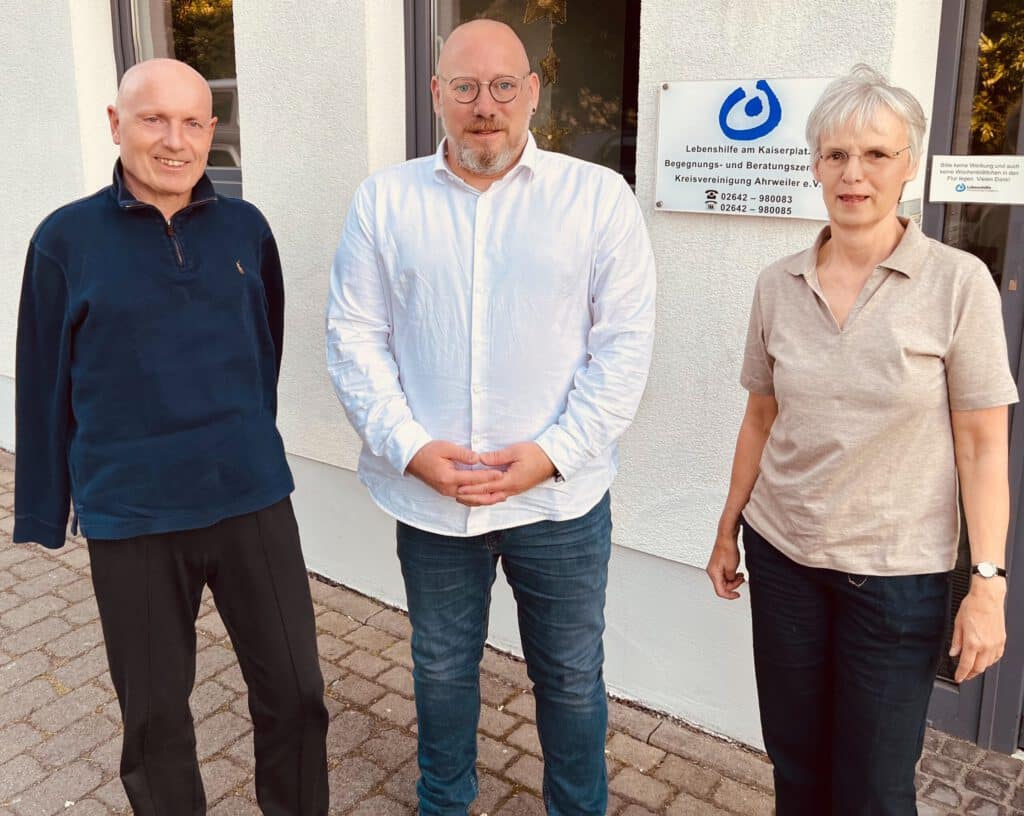 Drei Erwachsene stehen vor einem Gebäude neben einem Schild für ein Beratungs- und Unterstützungszentrum.