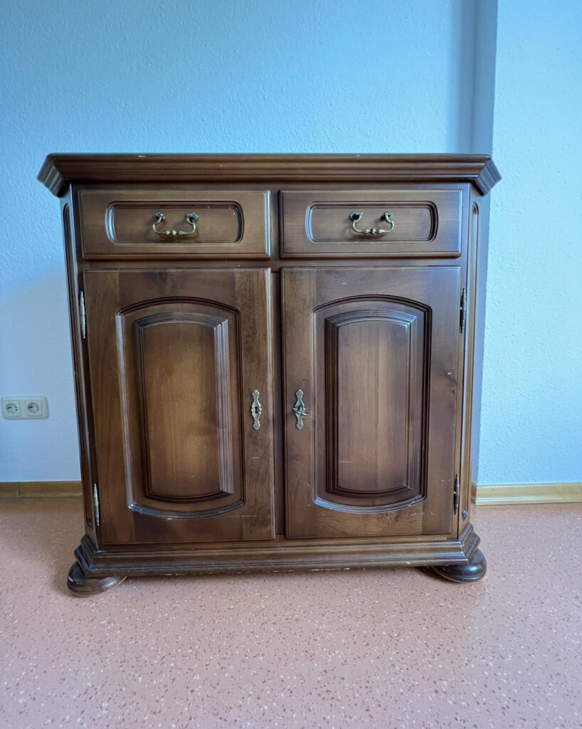 Ein Holzschrank mit zwei Schubladen und zwei Türen vor einer blauen Wand.