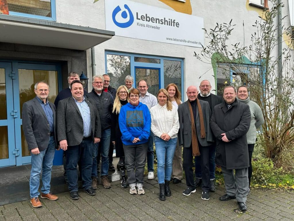 Eine Gruppe von Menschen steht lächelnd vor einem Gebäude mit einem Lebenshilfe-Schild.