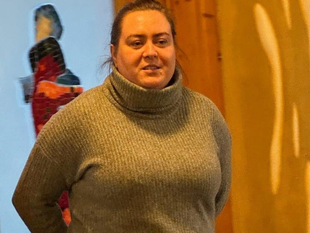 Person im grauen Rollkragenpullover, die in einem Haus mit unscharfem Hintergrund steht.