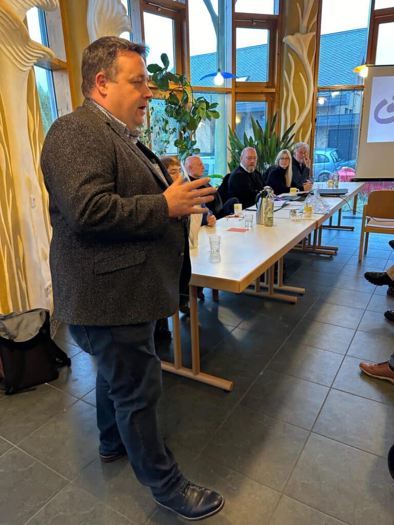 Ein Mann spricht zu den Zuhörern einer Podiumsdiskussion in einem Raum mit vier Personen, die an einem Tisch sitzen.