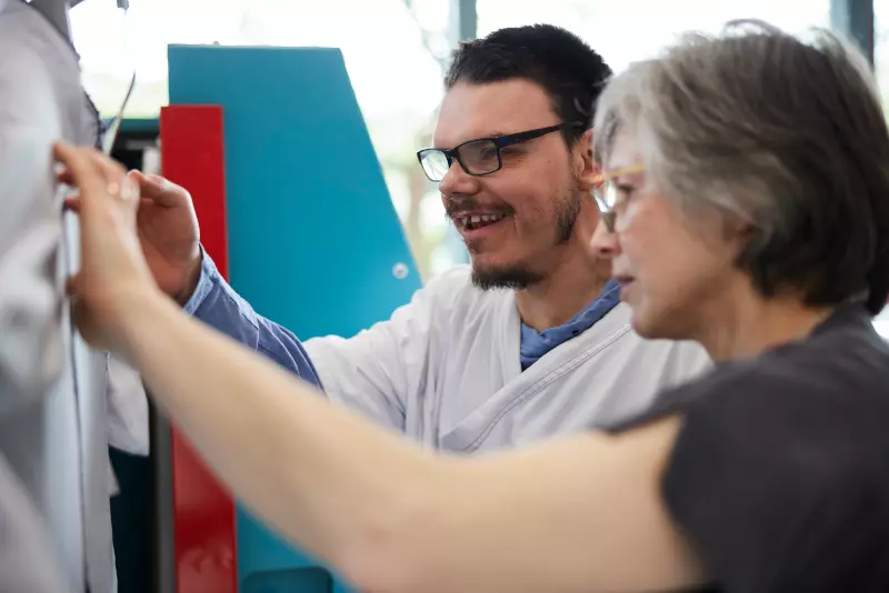 Zwei Personen arbeiten eng zusammen. Eine trägt eine Brille und einen weißen Kittel. Beide konzentrieren sich auf eine vor ihnen liegende Aufgabe und arbeiten möglicherweise gemeinsam an einem Projekt oder einer Aktivität.