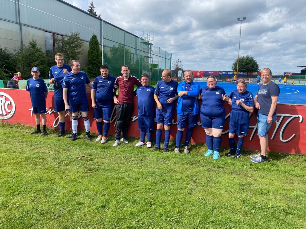 Eine Fußballmannschaft in blauen Trikots posiert an einem bewölkten Tag gemeinsam auf einem Feld.