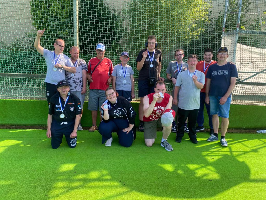 Eine Gruppe von Menschen posiert im Freien auf einem grünen Sportplatz und zeigt ihre Medaillen.