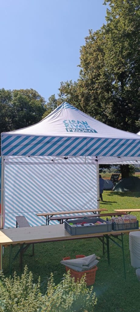 Weiß und blau gestreiftes Outdoor-Zelt mit Tischen und Zubehör auf einer Wiese.