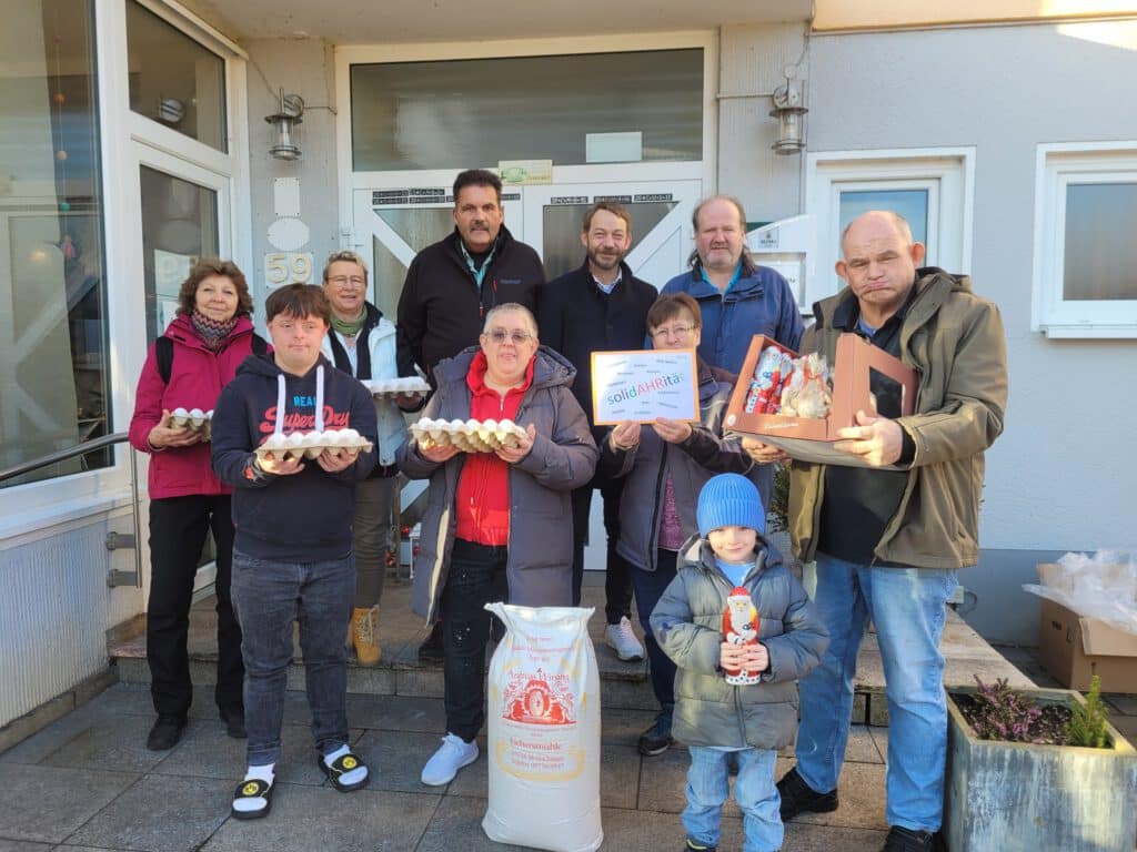 Eine Gruppe von Menschen posiert vor einem Gebäude und hält Eier, einen Kuchen und einen Sack Reis in der Hand.