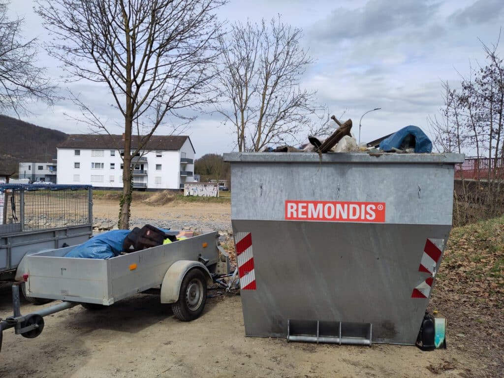 Ein Anhänger parkt neben einem großen Metallcontainer mit der Aufschrift Remondis im Freien.