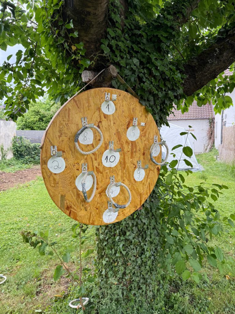 Hölzerne Zieltafel mit nummerierten Papierkreisen, die an einem Baum im Freien hängen.