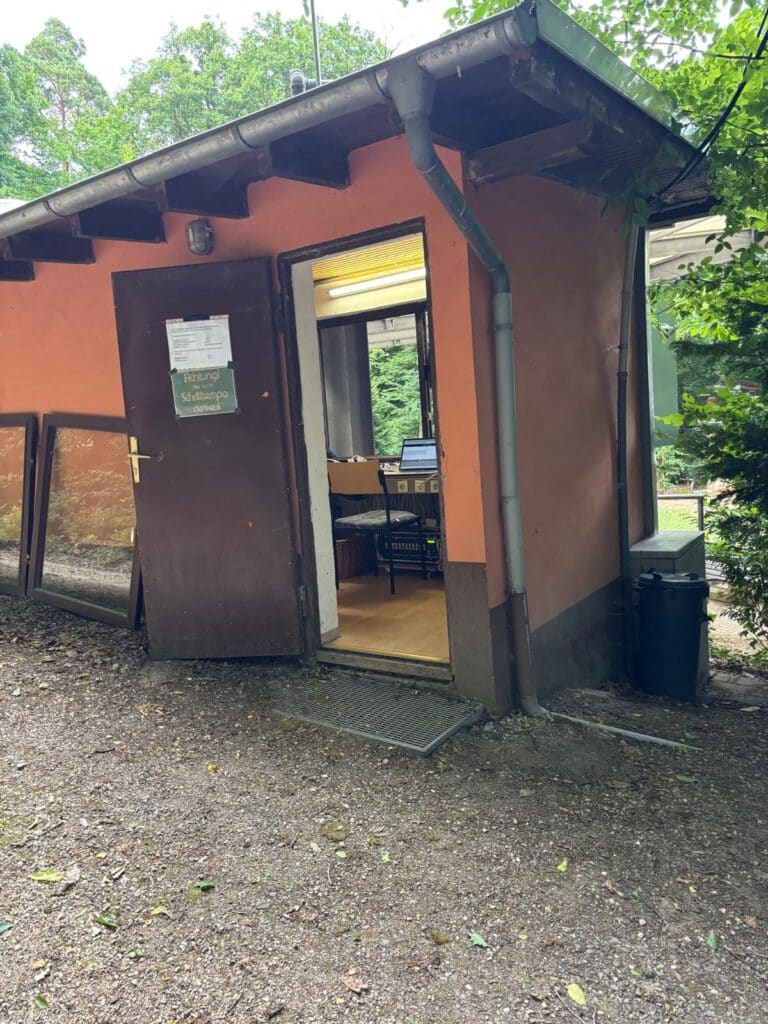 Kleines orangefarbenes Gebäude mit einer offenen Tür, die ein beleuchtetes Büro und einen Stuhl im Inneren zeigt.