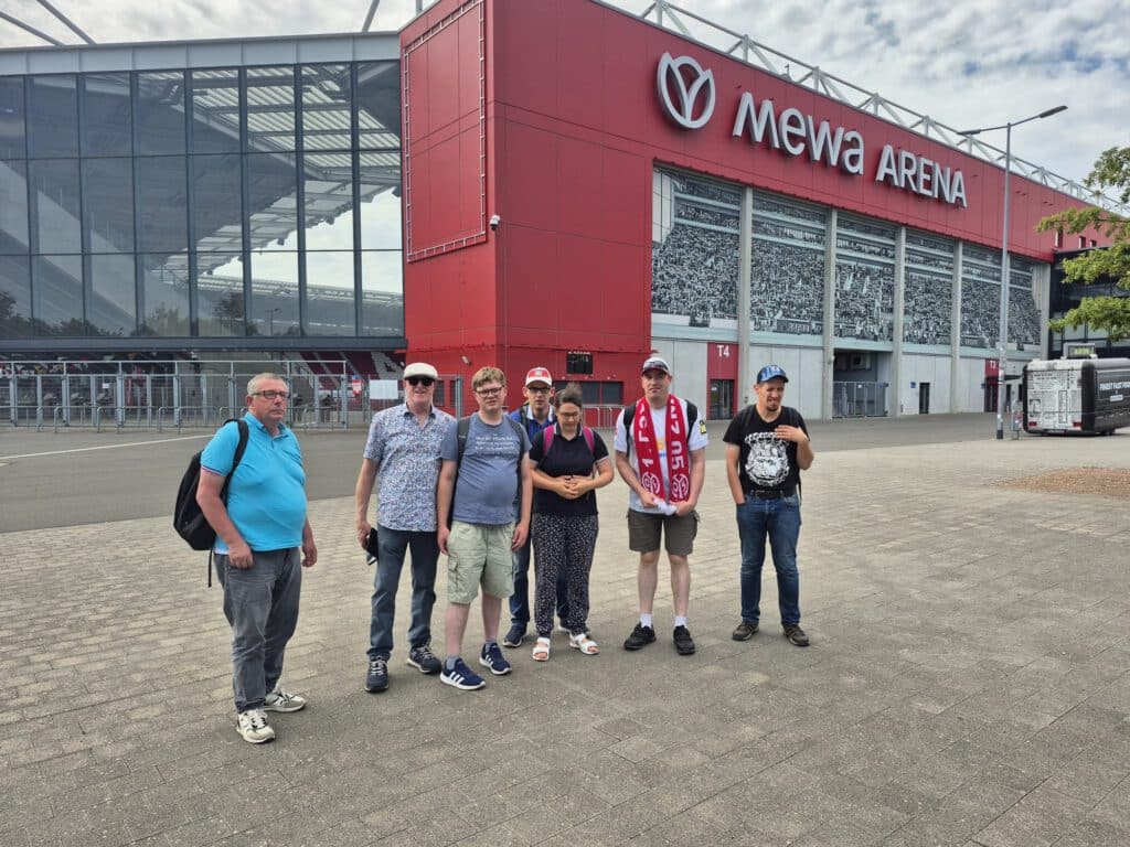 An einem bewölkten Tag stehen sieben Menschen vor dem Mewa-Arena-Stadion.