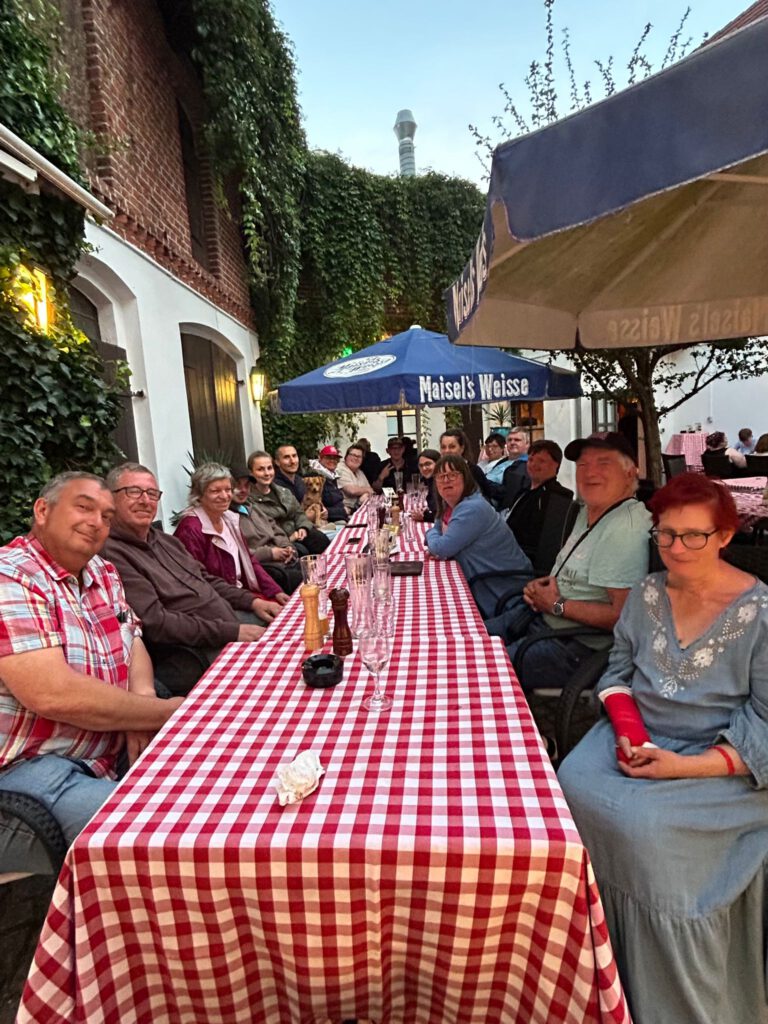 Eine große Gruppe von Menschen sitzt im Freien an einem langen Tisch mit rot karierten Tischdecken.