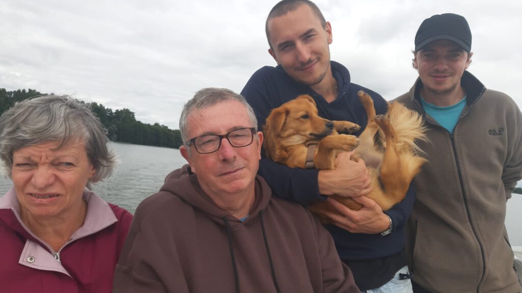 Vier Erwachsene und ein Hund posieren gemeinsam im Freien an einem See an einem bewölkten Tag.
