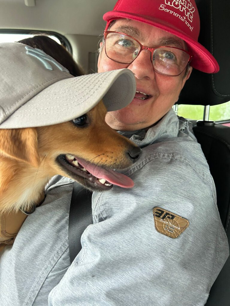 Eine Person und ein Hund, die beide Mützen tragen, sitzen zusammen in einem Auto und blicken beide in die Kamera.