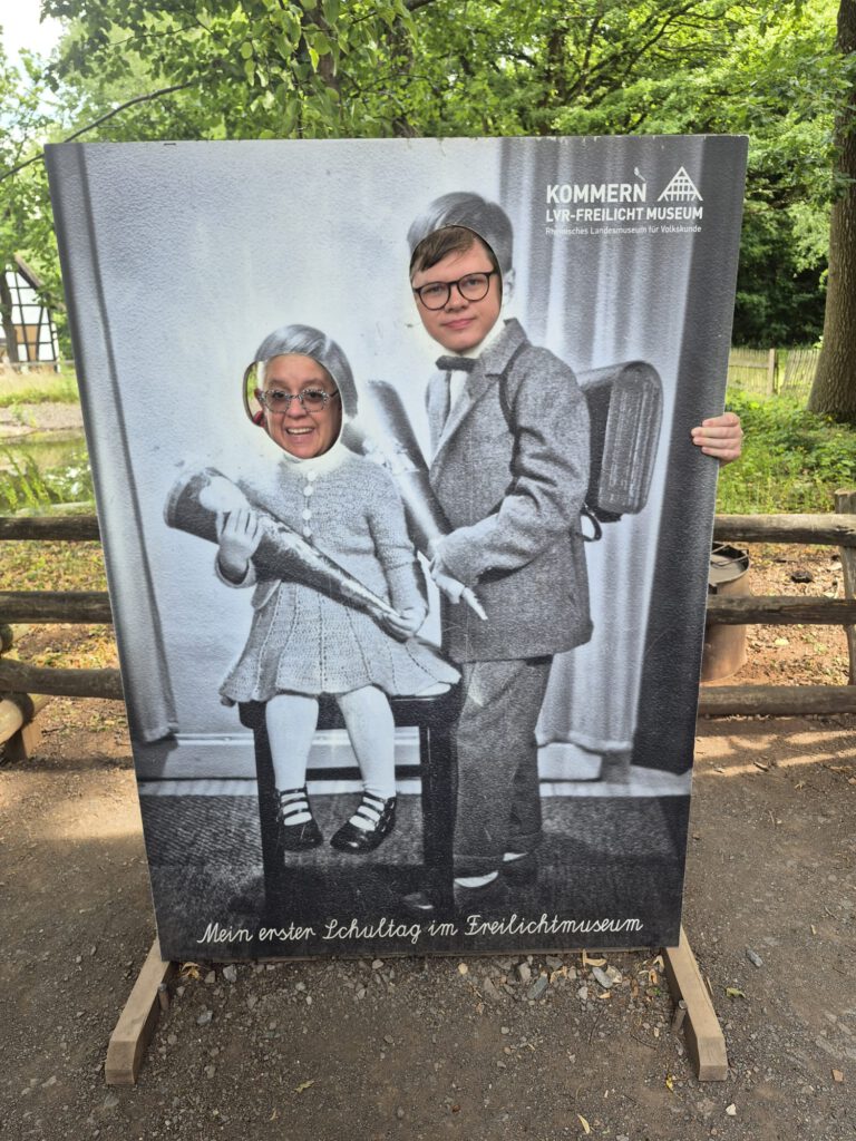 Zwei Personen posieren mit ihren Gesichtern in einer Ausschnittvorlage eines alten Schulfotos in einem Freilichtmuseum.