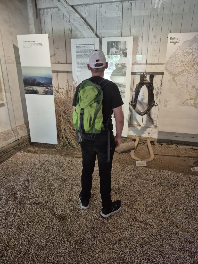 Eine Person mit einem grünen Rucksack betrachtet die Informationsdisplays in einer rustikalen Ausstellungshalle.