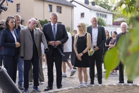 Eine Gruppe von Menschen in formeller und legerer Kleidung, die im Freien in der Nähe einer runden Steinumrandung stehen.