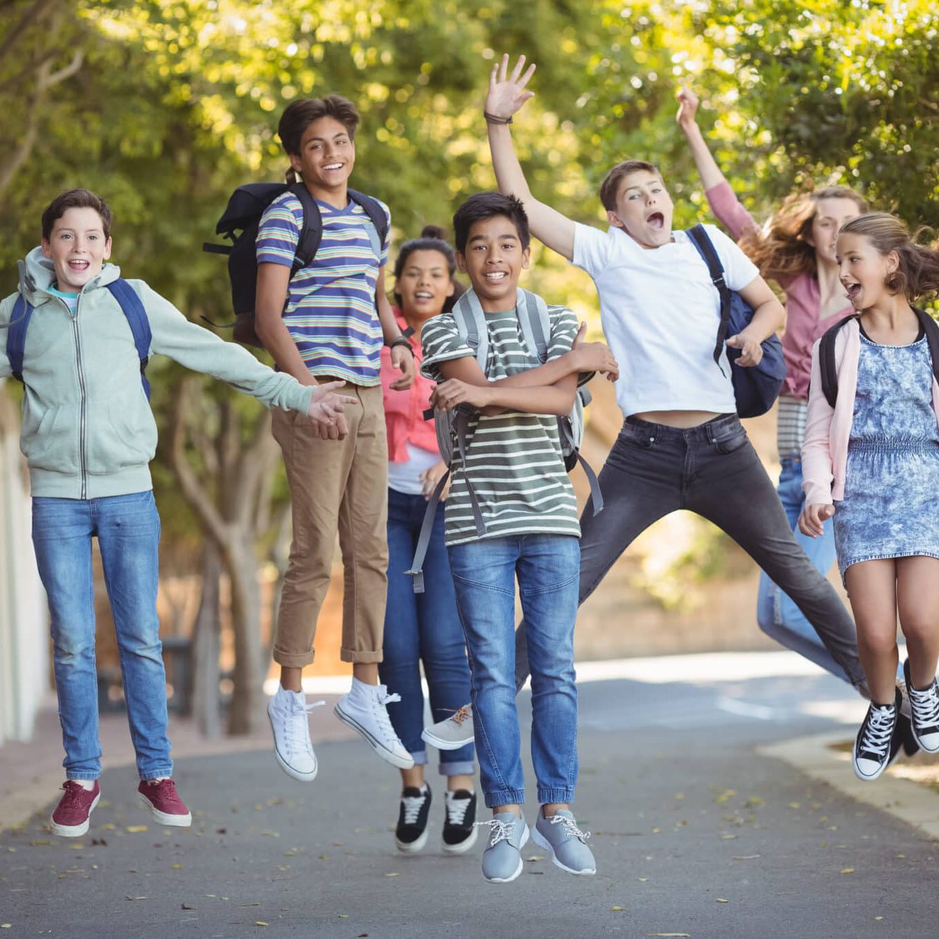 Eine Gruppe lächelnder Teenager mit Rucksäcken, die an einem sonnigen Tag im Freien herumhüpfen.