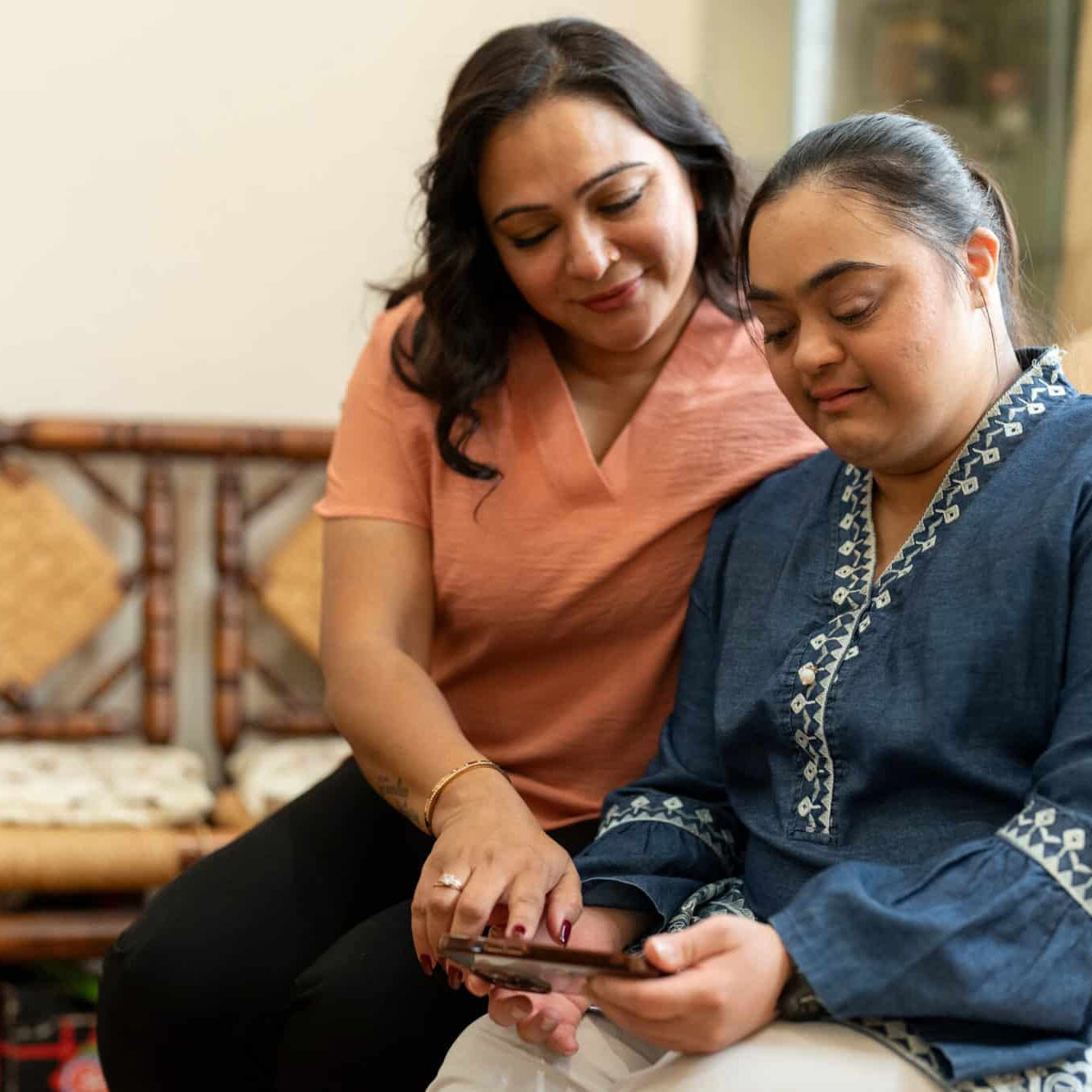 Zwei Frauen sitzen nebeneinander auf einem Sofa und schauen auf den Bildschirm eines Smartphones.